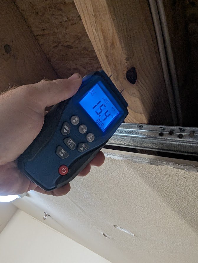 Pin moisture meter testing wood framing between apartment units during water damage drying in Bellingham, WA